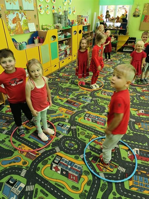 Na dywanie leżą hula - hop, w środku pojedynczo lub dwójkami stoją dzieci.
