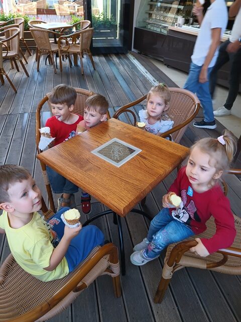 Dzieci siedzą przy stoliku w kawiarni i jedzą lody.