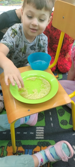 Chłopiec wkłada do miski z brokatem palec umoczony w mydle.