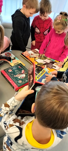 Dzieci oglądają książki wyłożone na dużym stole.