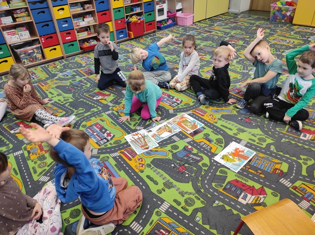 dzieci siedzą w kole na dywanie, jedna dziewczynka wybiera obrazek i układa  obok innych ilustracji
