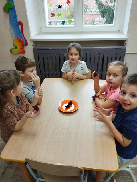 Dzieci siedzą przy stoliku i jedzą ugotowane buraki.