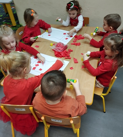 Przedszkolaki  wyklejają czerwona bibułą kontur mikołajkowej skarpetki. 