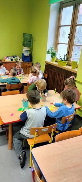 Dzieci przy stolikach ozdabiają wycięte z kolorowego papieru maski karnawałowe.
