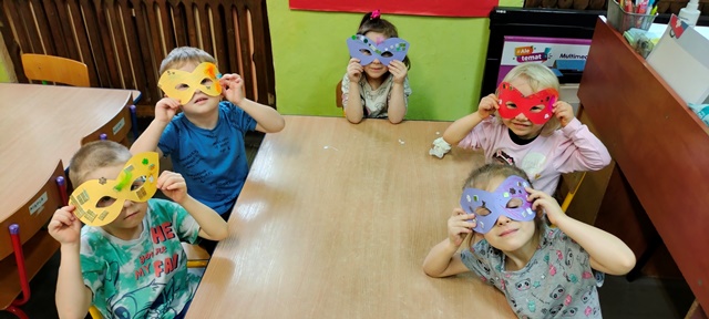 Dzieci przykładają do twarzy wykonane maski karnawałowe.