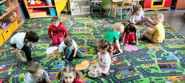 Dzieci na dywanie dopasowują do siebie dwa kawałki puzzli w kształcie serca.