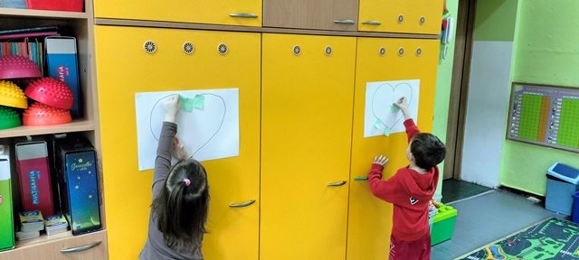 Dzieci przyklejają kolorowe karteczki do konturu serca narysowanego do dużym arkuszu papieru,