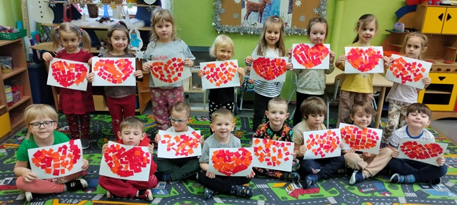 Grupa dzieci trzyma w rękach sylwety serc wyklejone kawałkami czerwonej i pomarańczowej bibuły.