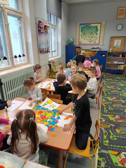 Dzieci przy stolikach wykonują obrazki z figur geometrycznych