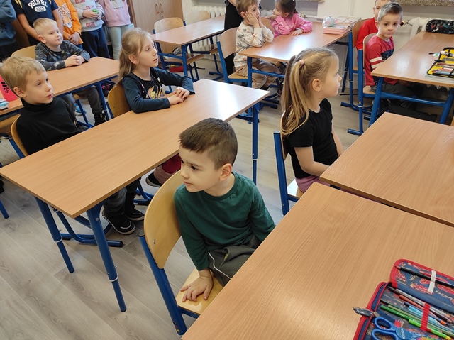 Dzieci siedzą w ławkach w sali lekcyjnej