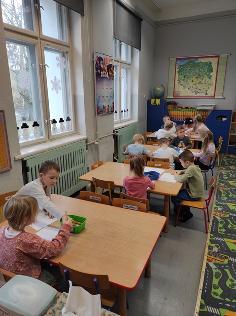 Dzieci siedzą przy stolikach i kolorują 