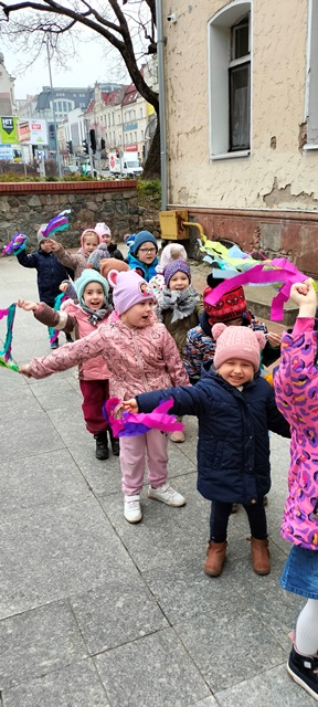Dzieci stoją parami i machają paskami kolorowej bibuły.