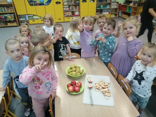 Dzieci stoją wokół stolika na którym znajdują się jabłka i gruszki przeznaczone do degustacji.  