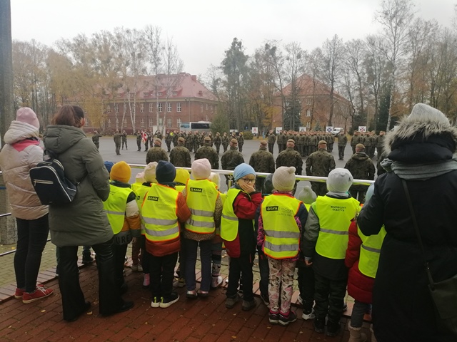 Dzieci stoją na trybunie i wspólnie z żołnierzami śpiewają hymn Polski