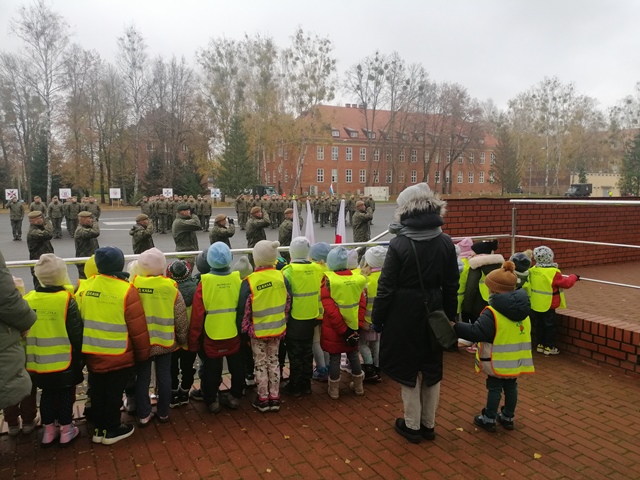 Dzieci stoją na trybunie i wspólnie z żołnierzami śpiewają hymn Polski