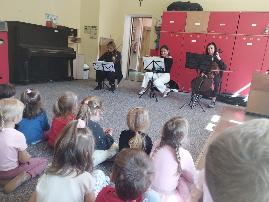Dzieci siedzą na dywanie, przed nimi muzycy z Filharmonii grający na instrumentach.