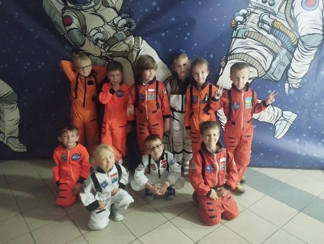 Dzieci w przebraniach astronautów pozują na ściance z kosmosem.