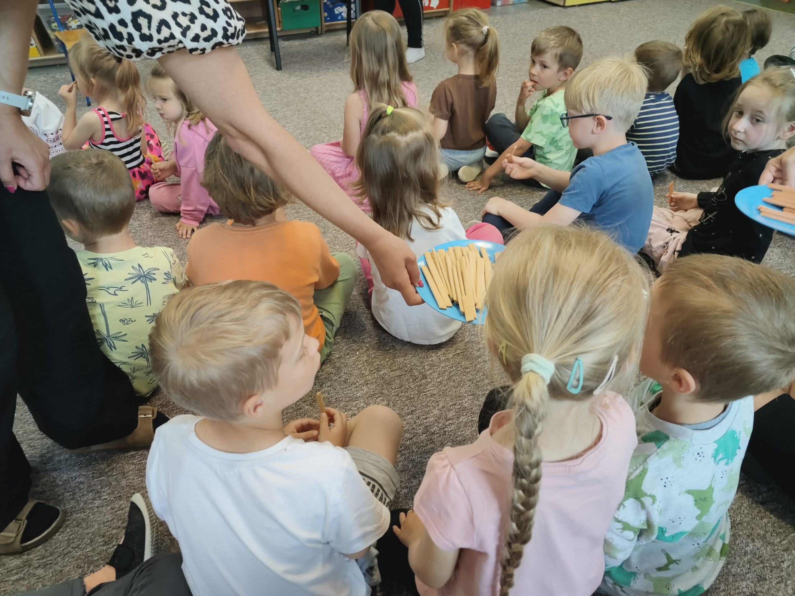 Dzieci siedzą na dywanie, częstując się ukraińskimi słodyczami.
